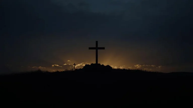 Silhouette of Jesus on the cross under a darkened sky at sunset, symbolizing the three hours of darkness during the crucifixion